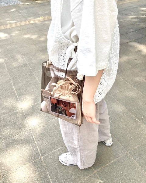 白でまとめた淡色コーデに好きなアイドルの写真が入ったクリアバッグを持った女性