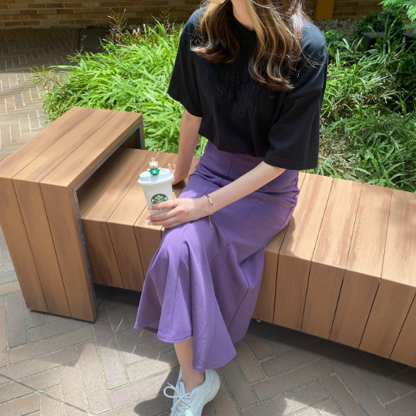 GUから展開されている「カットソーマーメイドロングスカート」の『パープル』を穿いて、ベンチに座っている様子
