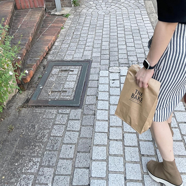 神戸にある海外風ベーカリー「THE BAKE」のテイクアウト紙袋を持った女性