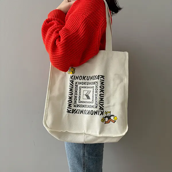 『リンネル』2024年6月号の付録「KINOKUNIYA×OSAMU GOODS」のショッピングバッグを持つ女性