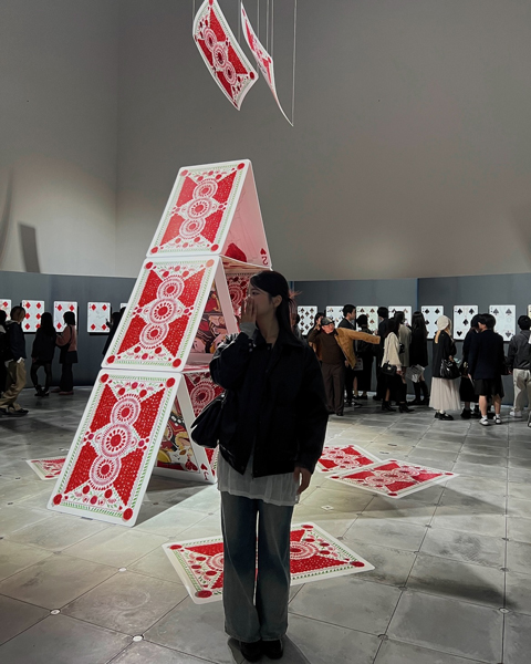 大阪・グラングリーン大阪内にある「VS.（ヴイエス）」にて開催中の吉田ユニさんの展示「PLAYING CARDS」で展示されているトランプタワーをバックに写真を撮っている女性